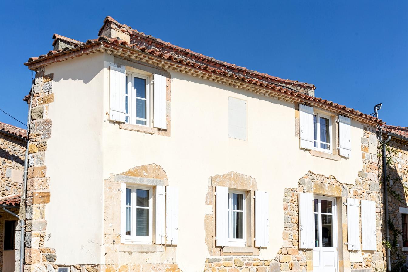 Façade de maison de village ravalée, enduit crème et entourages en pierre